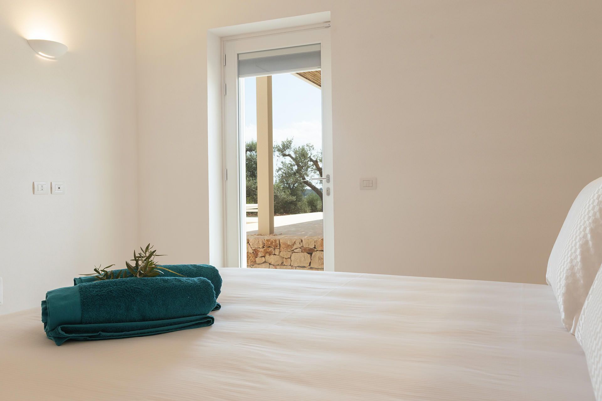 Un dormitorio con cama, una puerta que da a un espacio exterior y una planta pequeña sobre la cama.