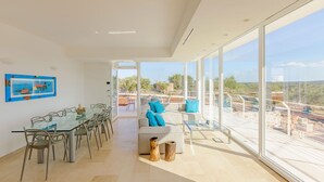 A spacious living area with a glass dining table, a sofa, and a view of a pool and landscape. - My Rental Homes - Villa Panita with swimming pool private garden wifi (Ostuni)