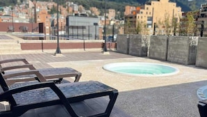A rooftop terrace with lounge chairs and a swimming pool, overlooking a cityscape and mountains. - ApartaSuite Spa Work Bogota  (Bogotá)