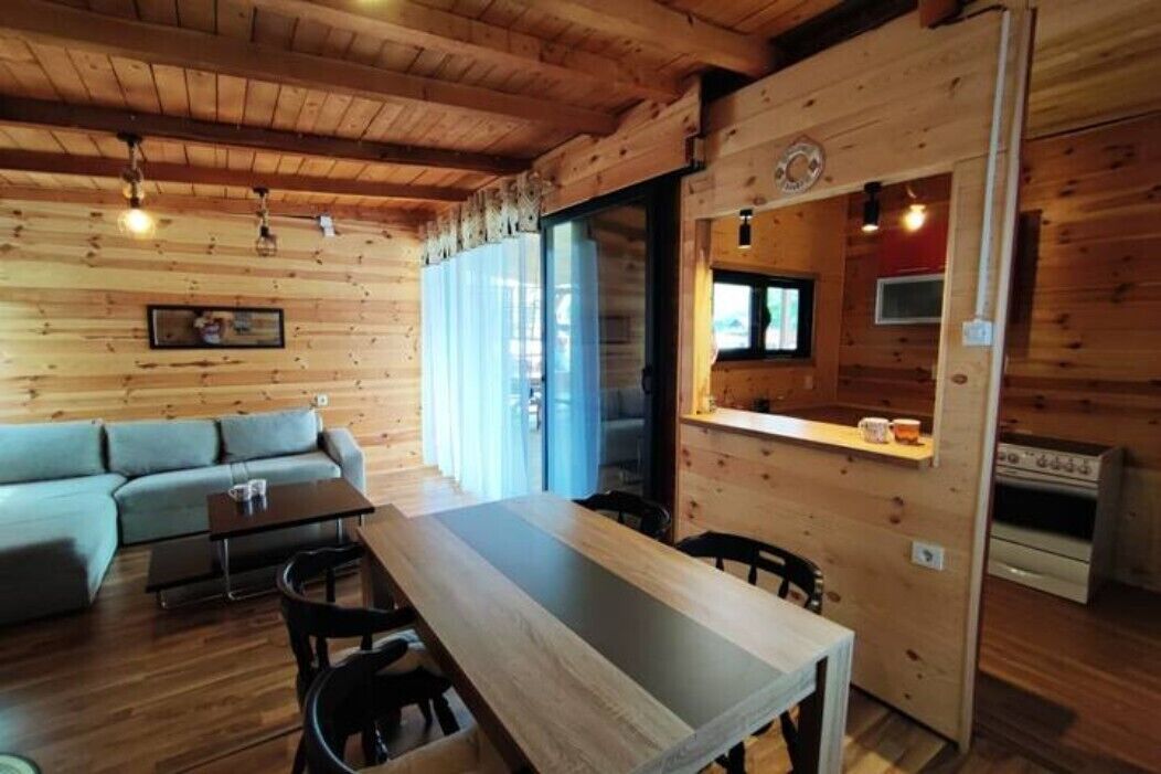 A cozy cabin interior with a wooden dining area, a sofa, and a kitchen with a stove.