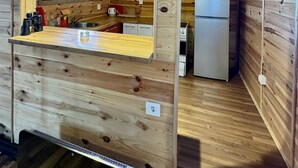 Interior de una cabaña de madera con cocina, que incluye un refrigerador, armarios y una encimera de madera.