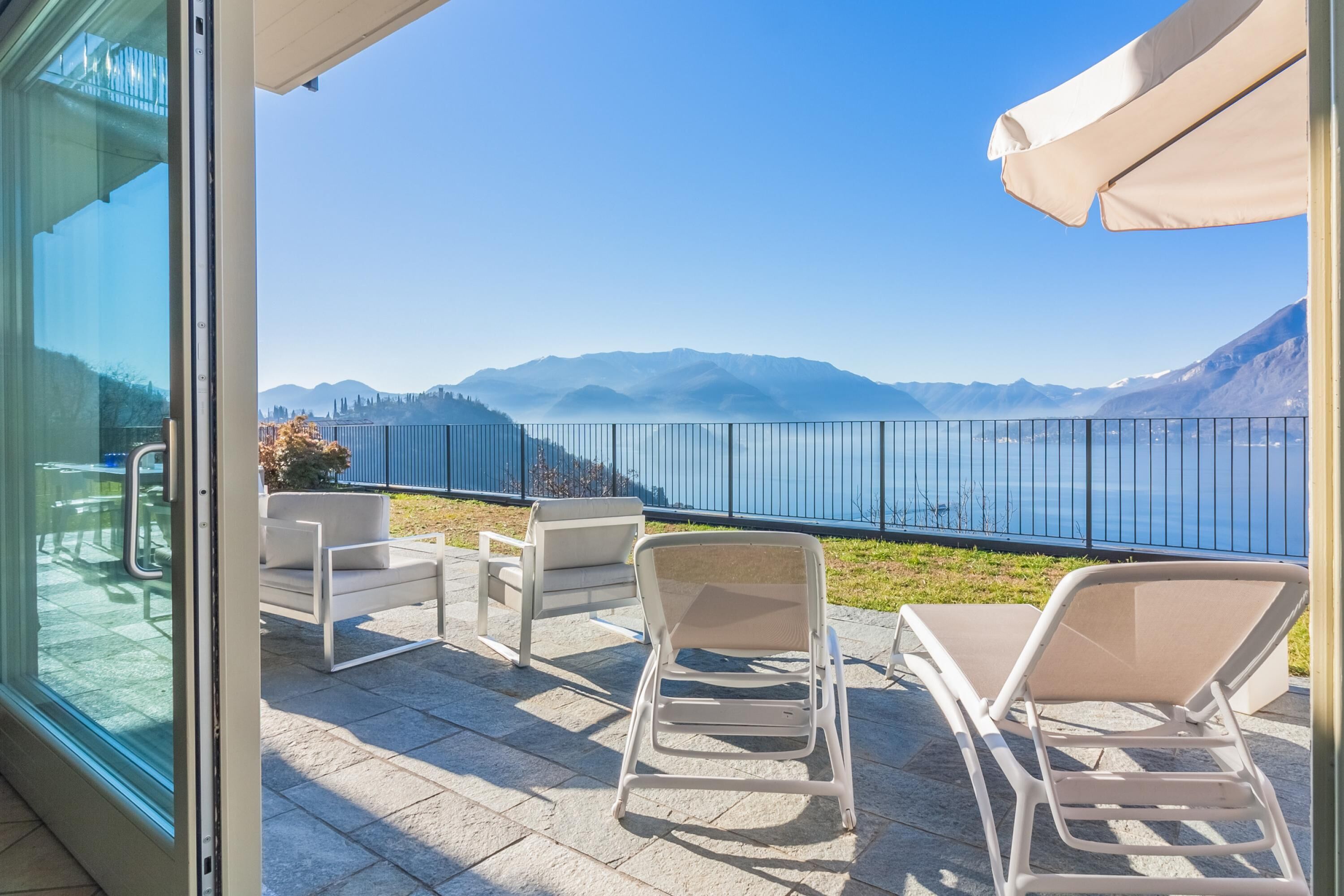 Een balkon met uitzicht op een meer en bergen, met twee loungestoelen en een tafel.