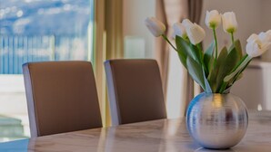 A dining table with a vase of white tulips, two brown chairs, and a view of the outdoors through a window. - The Patio Over Varenna (Perledo)