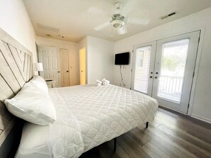 A bedroom with a large bed, a ceiling fan, a TV mounted on the wall, and a sliding glass door leading to a balcony. - Spacious duplex, short walk to the beach, shared Pool (North Myrtle Beach)