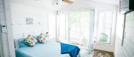Un dormitorio con cama, ventilador de techo, ventana y puerta.