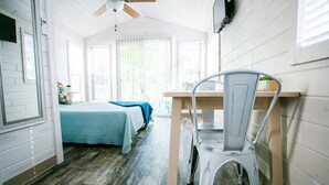 Une pièce comprenant un lit, un bureau et une chaise. Il y a une fenêtre avec des stores, un ventilateur de plafond et une porte.