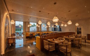A spacious restaurant with high ceilings, multiple dining areas, and a central seating area with a view of the outdoors. - Palm Springs Resort (Nashik)