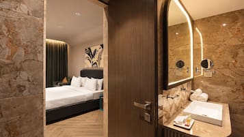 Quarto de hotel com cama, banheiro com um espelho grande e parede de mármore.