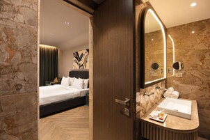 Quarto de hotel com cama, banheiro com um espelho grande e parede de mármore.