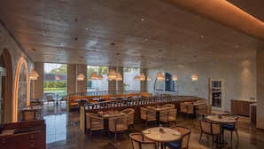 A spacious restaurant with high ceilings, wooden furniture, and large windows offering views of the outdoors. - Palm Springs Resort (Nashik)