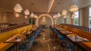A restaurant with booths and tables, a bar area, and a decorative wall with a circular pattern. - Palm Springs Resort (Nashik)