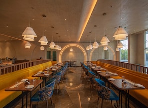 A restaurant with booths and tables, a bar area, and a decorative wall with a circular pattern. - Palm Springs Resort (Nashik)