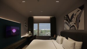 A modern hotel room with a large bed, a TV on the wall, a desk with a lamp, and a view of the city through the window. - Palm Springs Resort (Nashik)