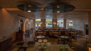 A spacious restaurant with high ceilings, large windows, and a variety of seating arrangements including tables and booths. - Palm Springs Resort (Nashik)