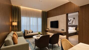 Quarto de hotel com sofá, cadeiras, escrivaninha, televisão e cama.