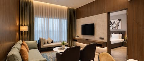 Ein Hotelzimmer mit einer Couch, Sesseln, einem Schreibtisch, einem Fernseher und einem Bett.