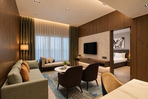 A hotel room with a sofa, chairs, a desk, a TV, and a bed. - Palm Springs Resort (Nashik)