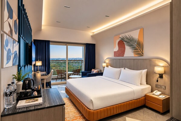A hotel room with a large bed, bedside tables, a desk with a chair, a balcony with a view, and artwork on the walls.