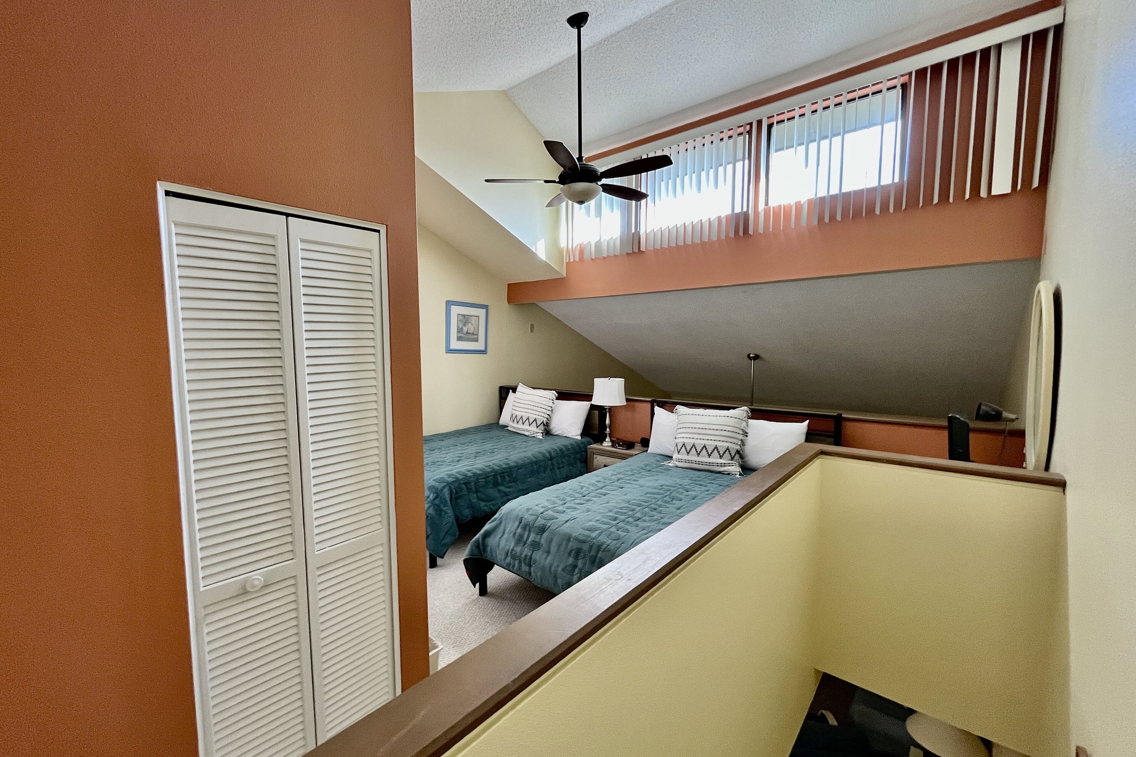Ein Schlafsaalzimmer mit zwei Einzelbetten, einem Deckenventilator, einem Fenster mit Jalousien, einem Schreibtisch und einem Kleiderschrank.
