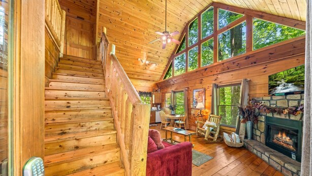 A wooden cabin interior with a staircase, a fireplace, and a dining area. - Fallin' in Love: Lose Your Heart in the Smokies (Sevierville)