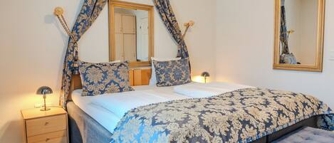 A bedroom with a bed, a nightstand, a bench, a mirror, and curtains.