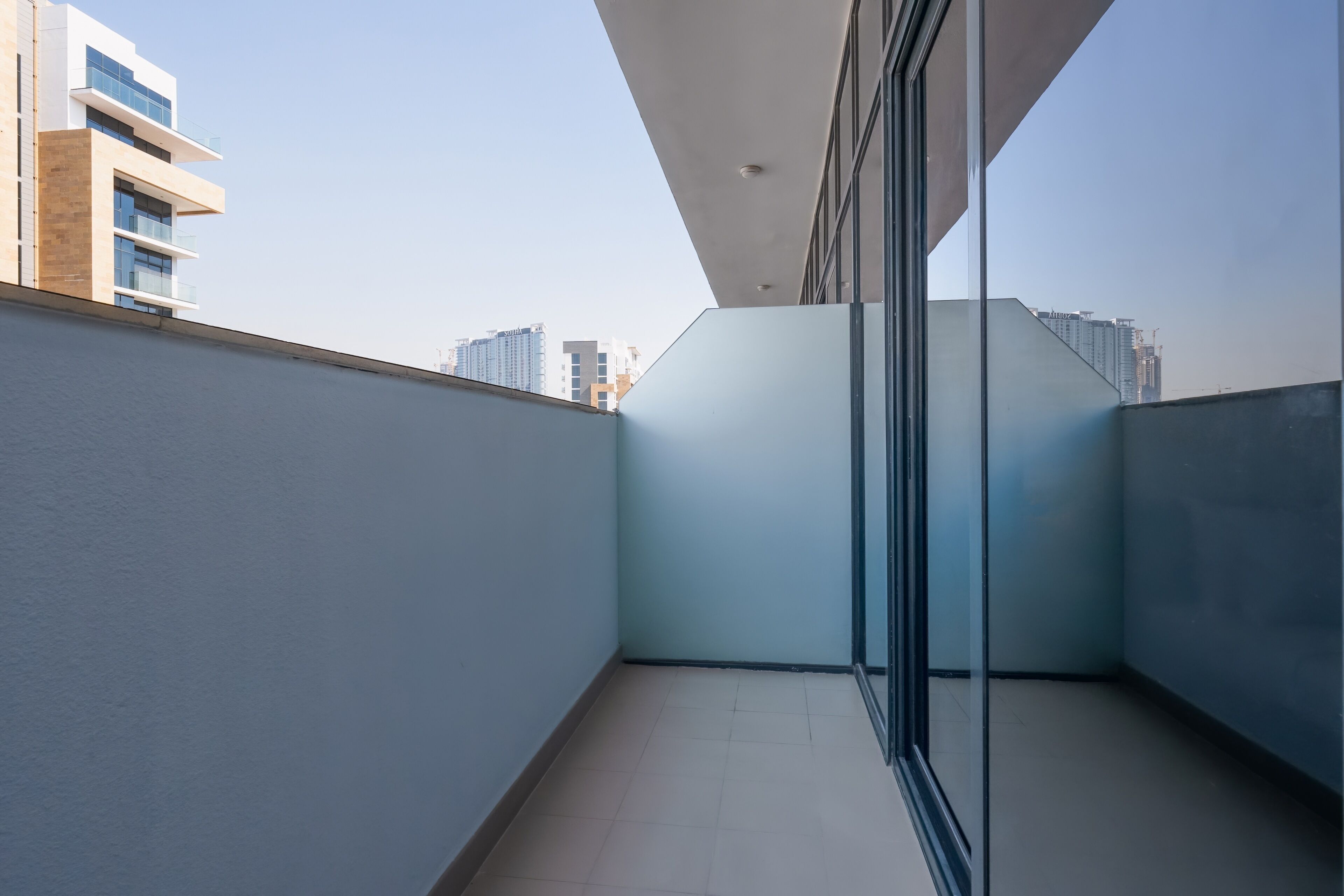 A modern balcony with a glass door, a clear view of the cityscape, and a tiled floor.