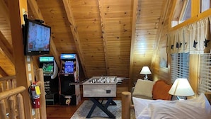 A cozy room with a foosball table, a television, and a small bar area with arcade games. - Cabin for 4 • Hot Tub • Jetted Tub • Arcade Loft (Sevierville)