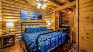 A log cabin bedroom with a bed, two wall-mounted lamps, and a ceiling fan. - Cabin for 4 • Hot Tub • Jetted Tub • Arcade Loft (Sevierville)