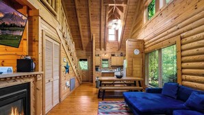A log cabin interior with a fireplace, a sofa, a dining table, and a kitchen area. - Cabin for 4 • Hot Tub • Jetted Tub • Arcade Loft (Sevierville)