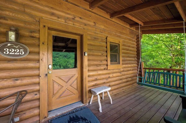 A log cabin with a wooden door, a small step leading to a porch, and a swing.