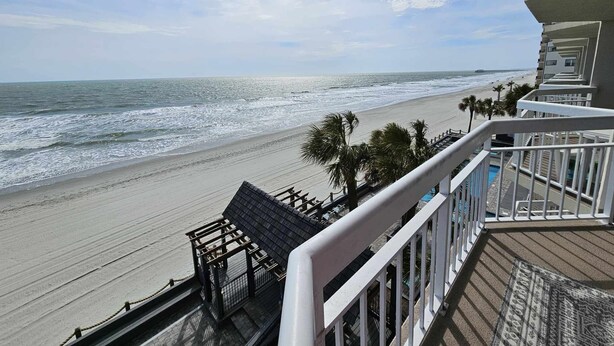 A beach view from a balcony with a wooden deck and a pool. - Garden City Beach Oceanfront Condo 306 | Rising Tides Properties Rental (Murrells Inlet)