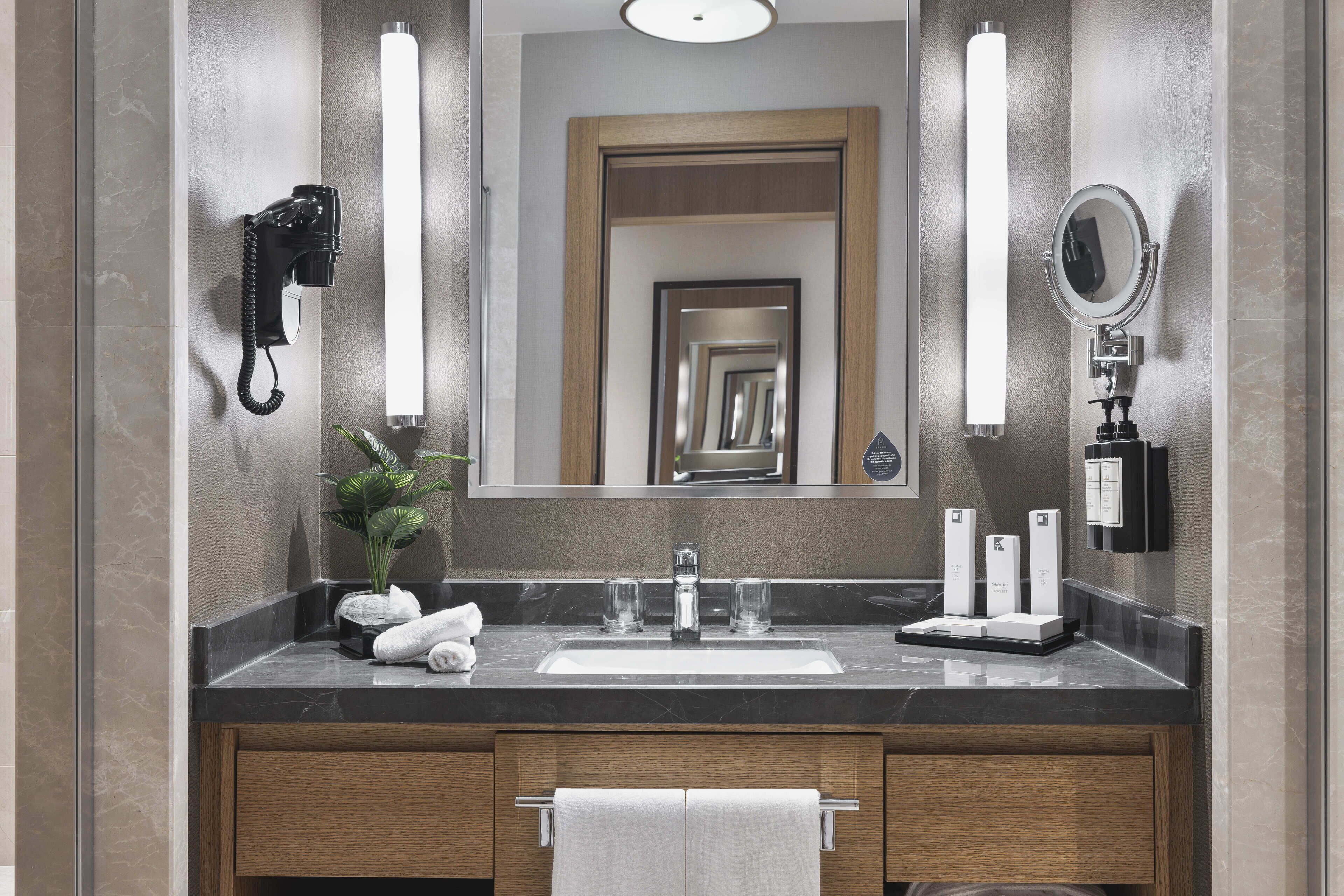 Un baño moderno con encimera de mármol, un espejo grande, un secador de pelo y un perchero.