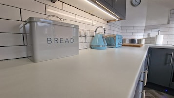 A kitchen with white tiles, a bread container, a kettle, and a toaster.