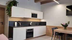 A modern kitchen with white cabinets, a black countertop, and a built-in microwave. There is a dining area with a table and chairs, and a TV mounted on the wall. - Magnolia LevicoGround floor apartment in the center of Levico Terme (Levico Terme)