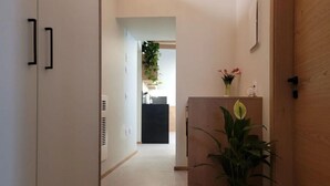 A hallway with a wooden door, a potted plant, and a small cabinet with a vase of flowers. - Magnolia LevicoGround floor apartment in the center of Levico Terme (Levico Terme)