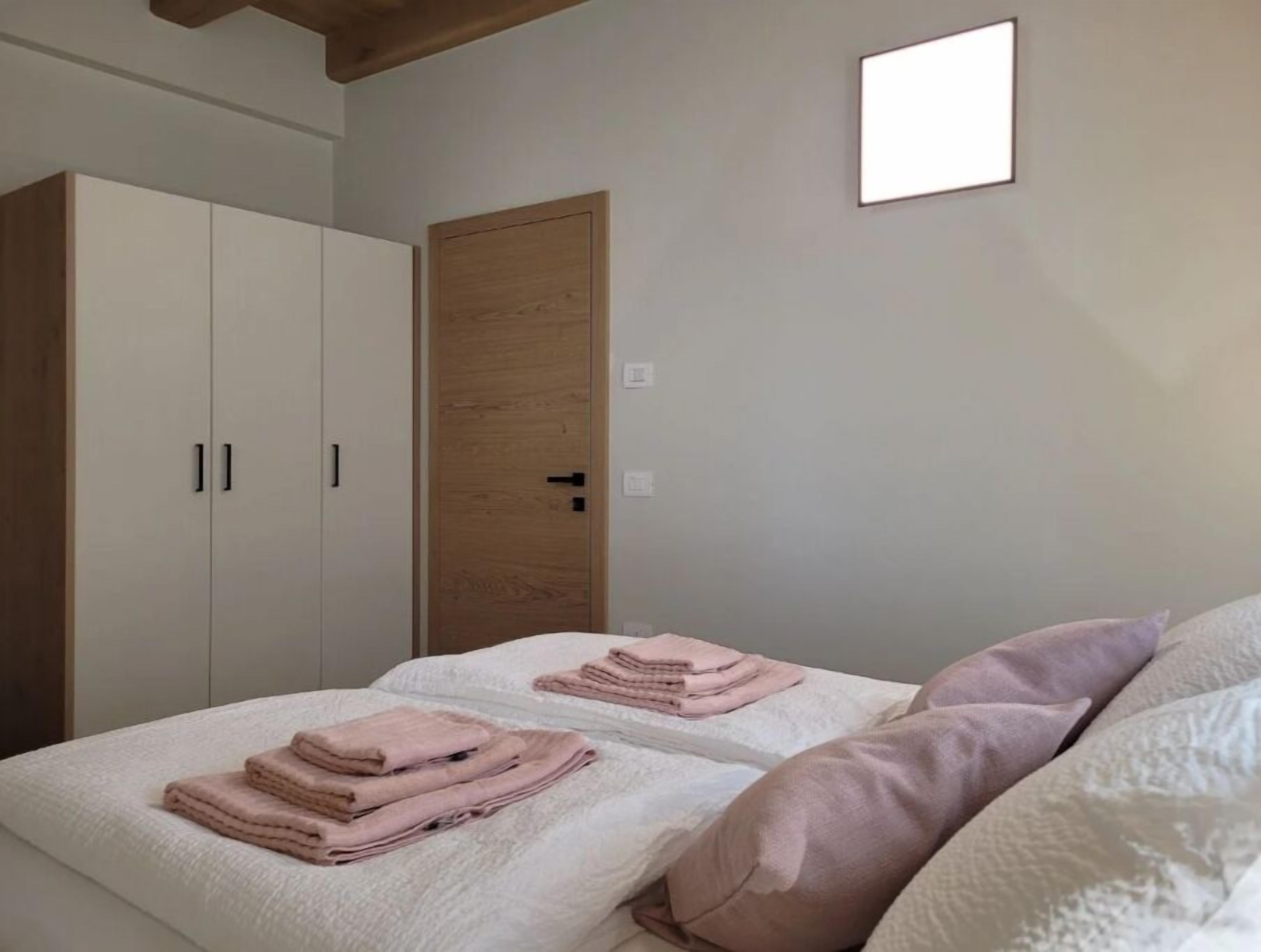 A bedroom with two beds, a wardrobe, a wooden door, and a wall-mounted light fixture.
