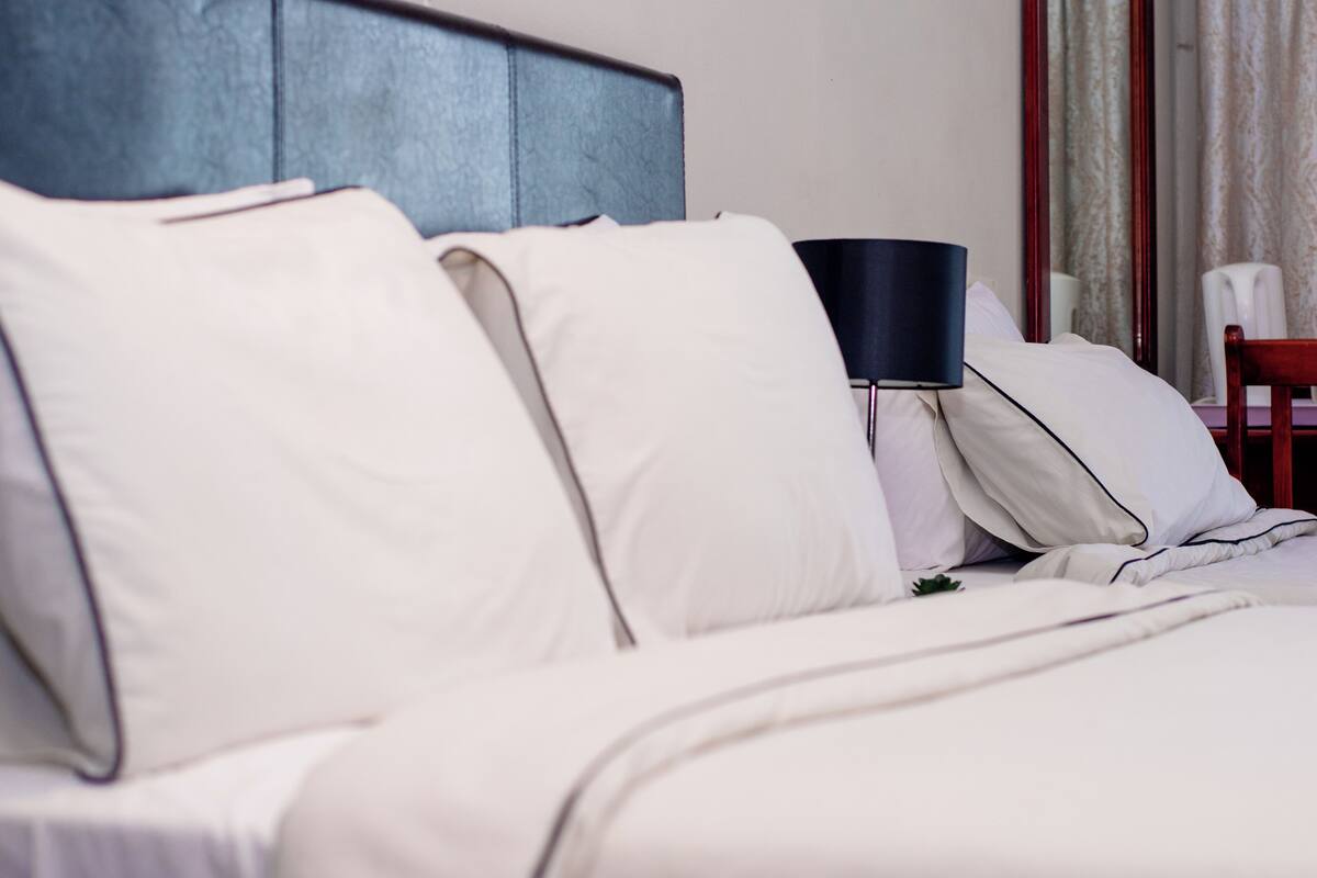 Een net opgemaakt bed met witte lakens en een donker hoofdbord.