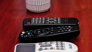 Two remote controls on a wooden surface with a potted succulent in the background.