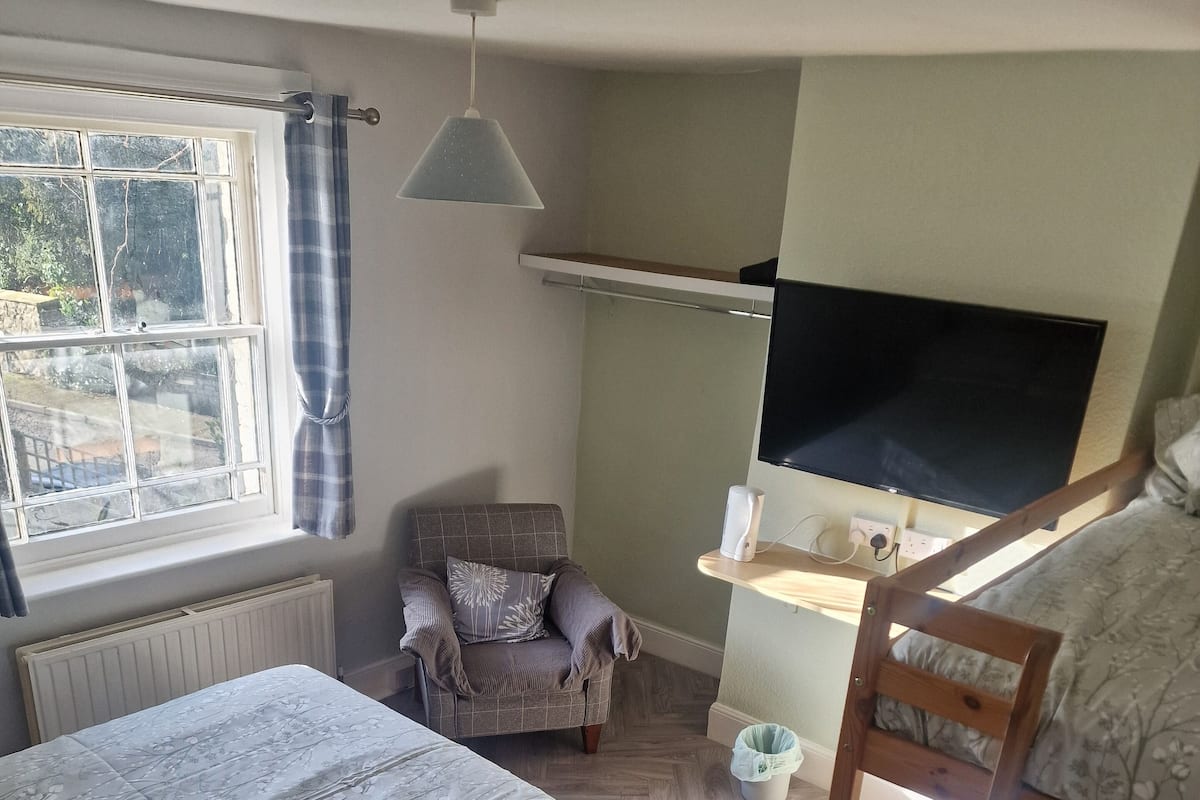 Une chambre avec deux lits, une chaise, un téléviseur et une fenêtre avec des rideaux.
