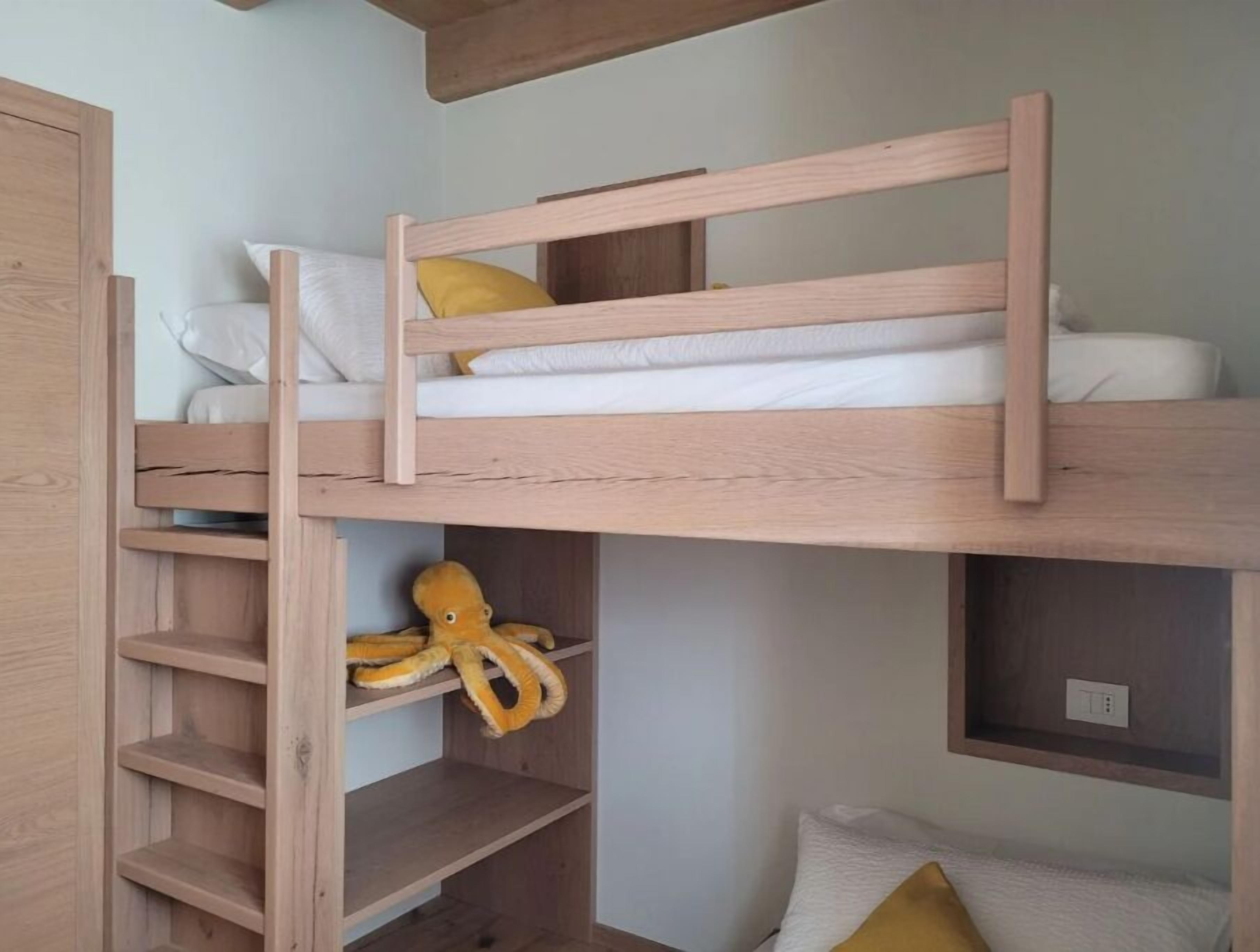 Un lit superposé avec une structure en bois, une étagère en dessous et une étagère fixée au mur sur laquelle se trouve un objet jaune.