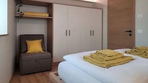 A bedroom with a bed, a chair, a wardrobe, and a shelf with a plant. - Magnolia LevicoApartment with terrace in the center of Levico Terme (Levico Terme)