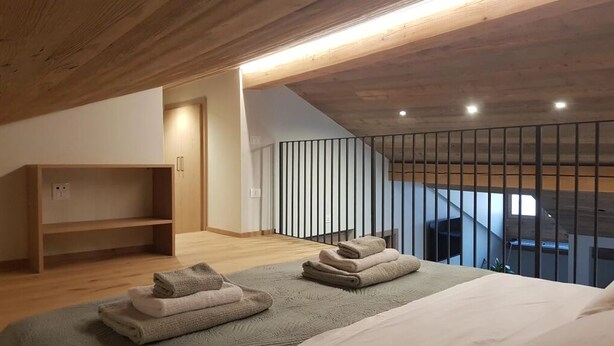 A bedroom with a wooden ceiling, a bed with folded towels, a wooden shelf, and a staircase with a railing.