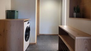 A laundry area with a washing machine, a trash bin, and a plant on a shelf.