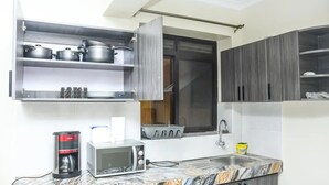 A compact kitchen with a microwave, coffee maker, and a shelf with pots. - IvyRose Luxury Apartment 1 (Kampala)