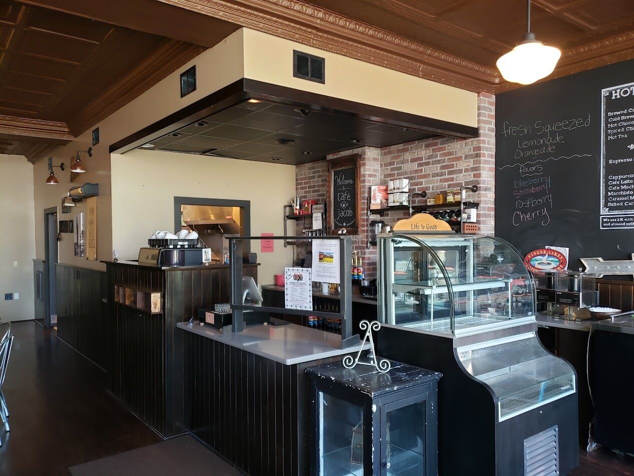Un interno di un caffè con un bancone, una lavagna con il menu e una macchina per il caffè.