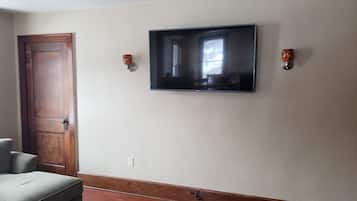 Une pièce avec une porte en bois, un téléviseur à écran plat fixé au mur et une petite table avec une chaise.