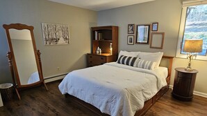 A bedroom with a wooden bed, a nightstand, a dresser, a mirror, and a window with a view. - Two bedroom + loft near Lake Leelanau. Fire pit, W/D, WIFI (Lake Leelanau)