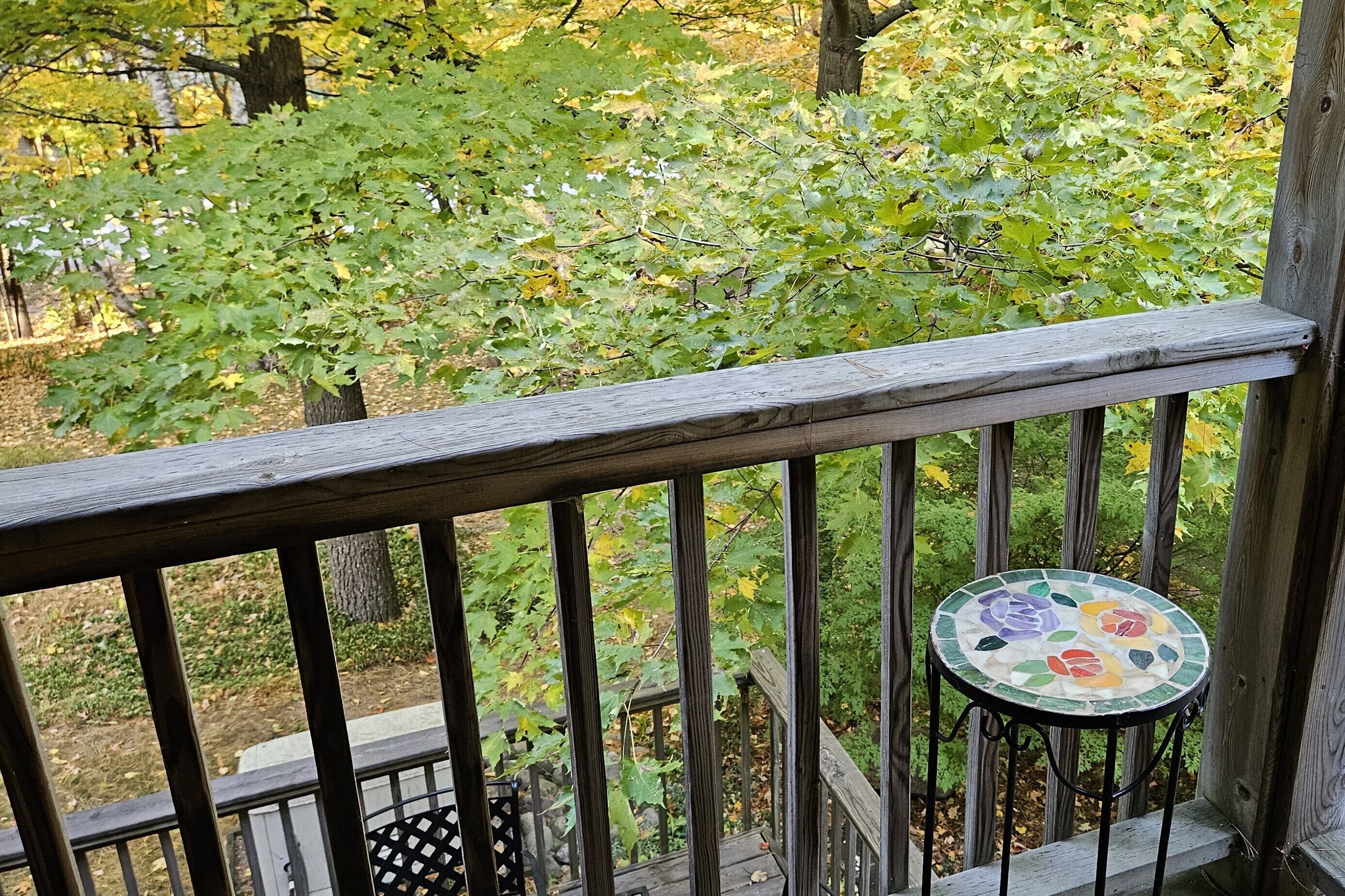 Une terrasse en bois avec une rambarde en métal et une petite table ronde ornée d’un motif floral coloré.