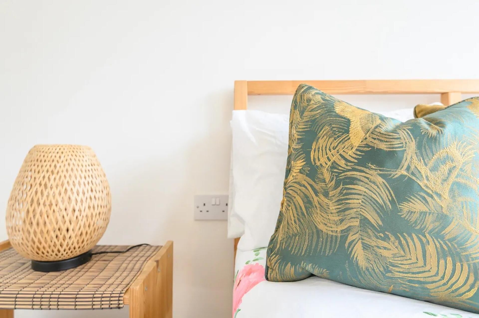 Un lit avec un coussin à motifs floraux et une lampe en osier sur une table de chevet.
