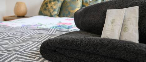 A neatly made bed with a patterned bedspread, a headboard with decorative pillows, and a package labeled 'eden' on a dark-colored sofa.